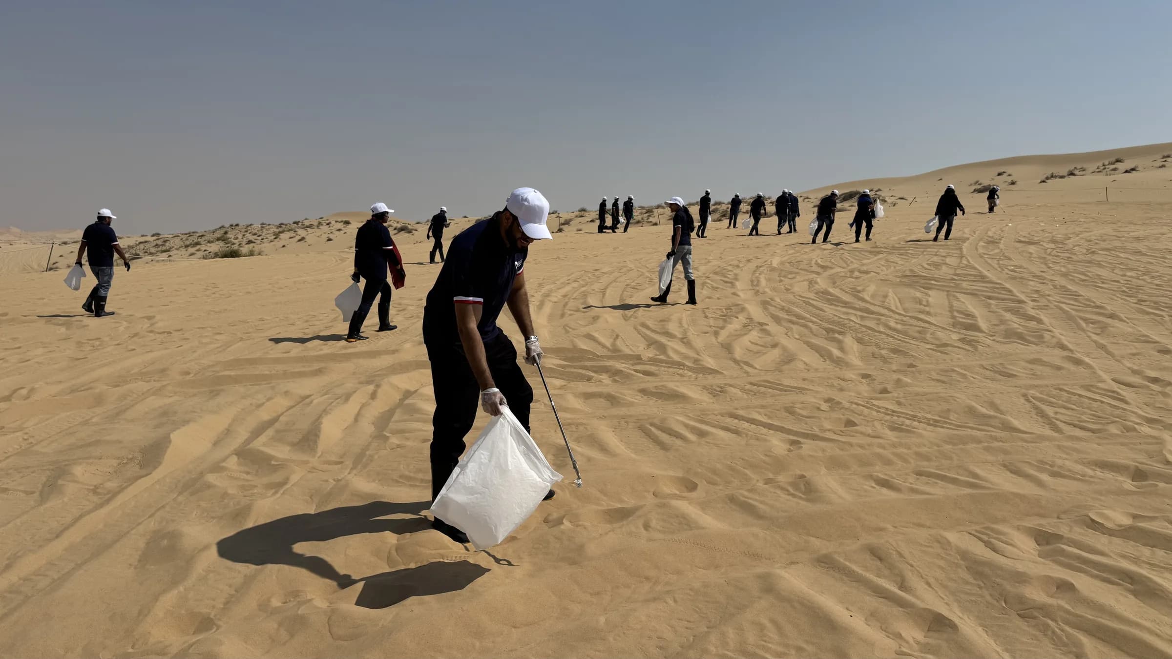 A Dolphin Group volunteer collecting waste into a bag on a desert dune